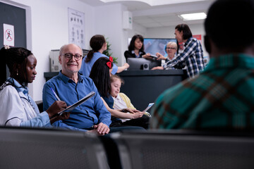 Portrait of older man with african american medical doctor looking at patient data while diverse...