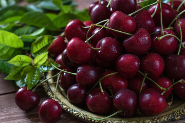 A metal vintage dish filled with cherries, cherry leaves nearby. Close-up.