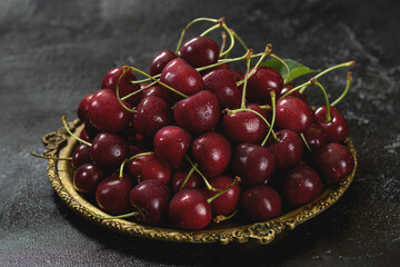 A metal vintage dish filled with cherries in the center. Dark background.