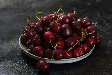 A white ceramic dish filled with cherries in the center. Dark background.