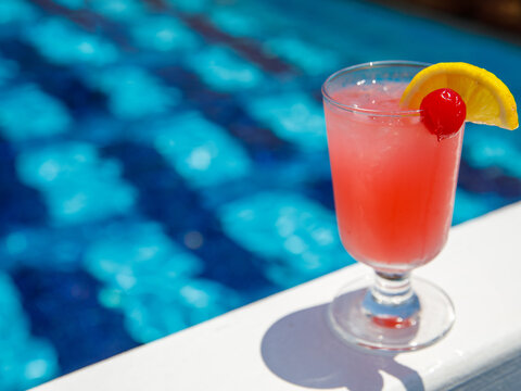 Glass of non alcoholic pink Strawberry lemonade cocktail on pool nosing at tropical resort. Horizontal, cocktail on right side. Healthy fresh cold drink. Pool cocktail party. Copy space