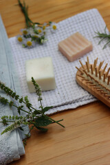 Zero waste cosmetics. Natural organic solid handmade shampoo soaps and mint, chamomile and rosemary plant near towels and wooden hairbrush on wooden table