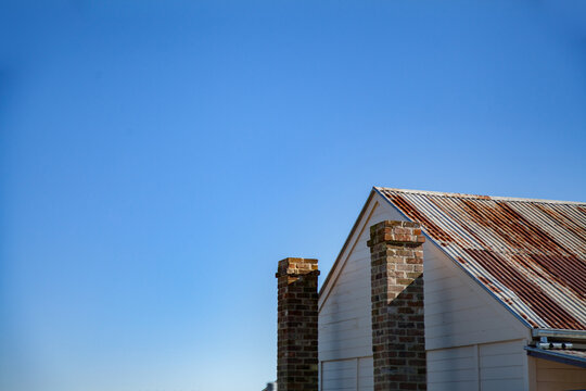 Rusty roof and stone chimney of old building against blue sky