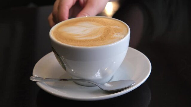 Female hand turns a cup of coffee with a beautiful latte art foam
