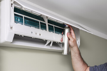 man cleaning home air conditioner with antibacterial spray