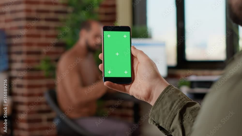 Poster startup worker using isolated greenscreen on mobile phone, looking at blank mockup display with copy