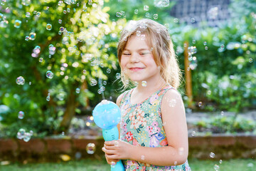 Happy little blonde preschool girl having fun with blowing soap bubble blower. Cute child playing on sunny summer day. Happy active funny healthy kid. Activity for children.