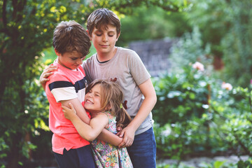 Portrait of three siblings children. Two kids brothers boys and little cute toddler sister girl having fun together in domestic garden. Happy healthy family playing, walking, active leisure on nature