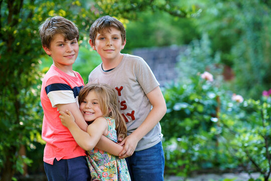 Portrait of three siblings children. Two kids brothers boys and little cute toddler sister girl having fun together in domestic garden. Happy healthy family playing, walking, active leisure on nature