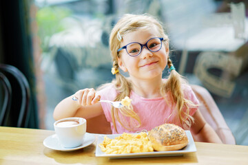 little smiling girl have a breakfast in a cafe. Preschool child with glasses drinking milk and...