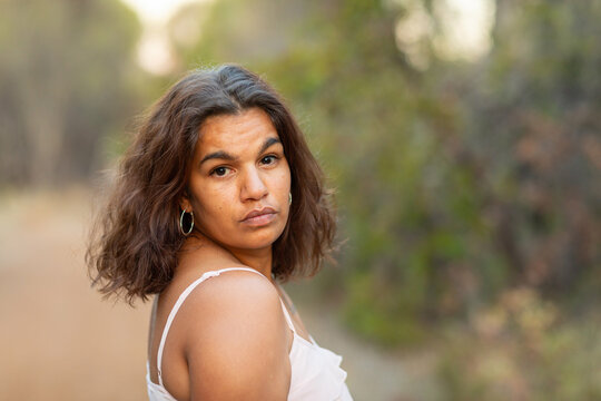 head and shoulders of dark haired lady looking over shoulder outdoors