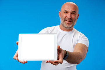 Happy caucasian middle-aged man showing tablet`s screen over blue background