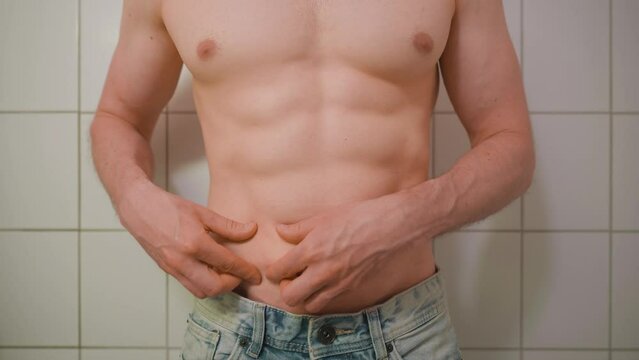 Shirtless man pinching his skin in a bathroom. Body image. Fitness. Obsession