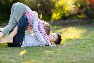 Brother and sister play fighting together on lawn in garden