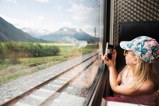 Girl on train taking photograph of mountains on smartphone