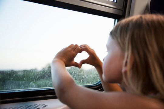 Girl making heart gesture by train window