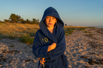 Boy in hooded bathrobe on beach at sunset