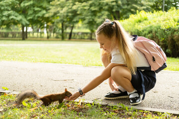 happy schoolgirl in uniform with backpack feeds a squirrel in the park on her way to school