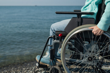 Naklejka premium Caucasian woman in a wheelchair on the seashore. Close-up of female hands.