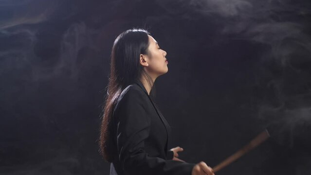 Side View Of Asian Conductor Woman Holding A Baton And Showing Gesture Quickly In The Black Studio With Fog 
