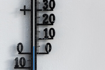 Classic black analog thermometer hanging on white wall displaying blue temperature scale of five, 5 degrees celsius