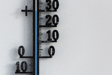 Classic black analog thermometer hanging on white wall displaying blue temperature scale of thirty, 30 degrees celsius
