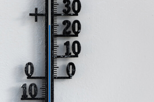Classic black analog thermometer hanging on white wall displaying blue temperature scale of twenty-five, 25 degrees celsius