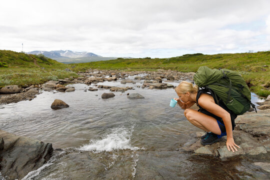 Woman drinking water from stream while hiking