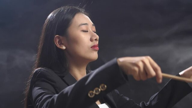 Close Up Of Asian Conductor Woman Holding A Baton Closing Her Eyes And Showing Gesture In The Black Studio With Fog 
