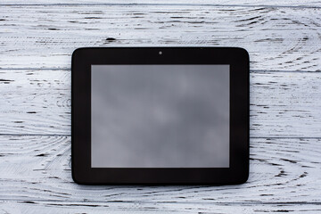 A black tablet with a blank display without an image lies on a light wooden textured surface