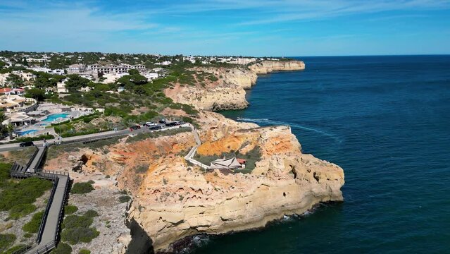 Drone flight over the cliffs near Boneca's Cave. A motorboat in the distance. Lagoa, Algarve, Portugal