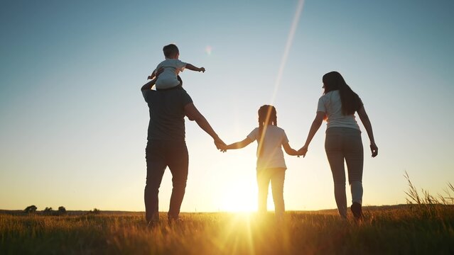 people in the park. happy family walking silhouette at sunset. mom dad and daughters walk holding hands in the park. happy family childhood sun dream concept. parents and children go back silhouette