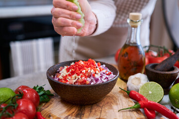 making salsa dip sauce - woman squeezing fresh lime juice to chopped ingredients in wooden bowl