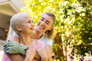 Image of happy diverse lesbian couple embracing in garden