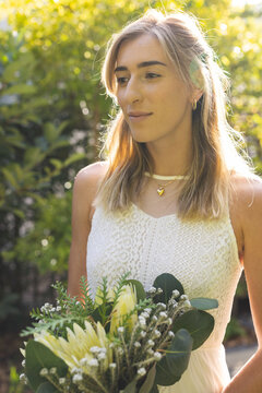 Vertical image of happy caucasian woman in wedding dress holding flowers
