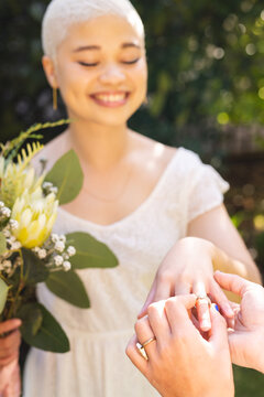 Image of happy biracial lesbian woman with wedding ring putting by her wife