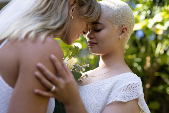 Image of diverse lesbian couple in wedding dresses embracing
