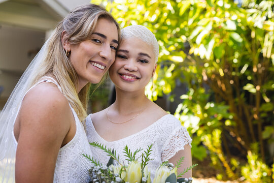 Image of happy diverse lesbian couple in wedding dresses
