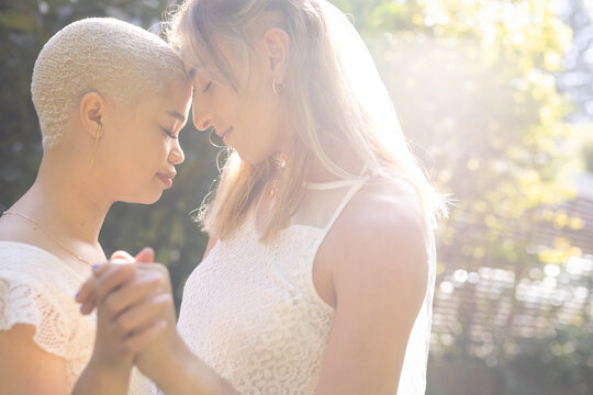 Image of happy diverse lesbian couple in wedding dresses dancing