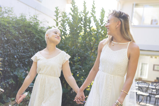 Image of happy diverse lesbian couple in wedding dresses holding hands