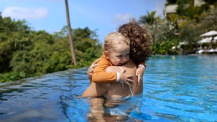 Love of mother and child. Mom hugs her baby tightly in the pool. Mom lovingly hugs her baby on vacation in the tropics. Slow motion video. The concept of love for their children moms.