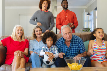 Excited multiracial multigeneration family watching soccer match on tv in living room