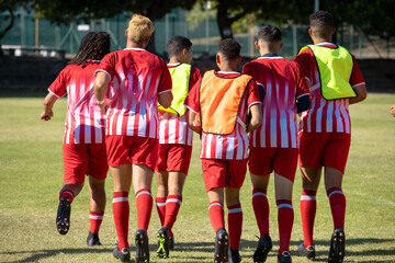 Obraz premium Rear view of multiracial male soccer players wearing red sports uniforms running at playground