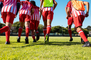 Low angle view of multiracial male athletes in red uniforms and soccer shoes running on grassy land