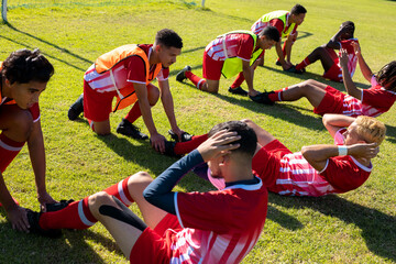 Obraz premium Multiracial male players holding legs of teammates practicing crunches on grassy field at playground
