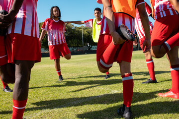 Obraz premium Male multiracial athletes in red uniforms stretching legs while exercising in playground in summer