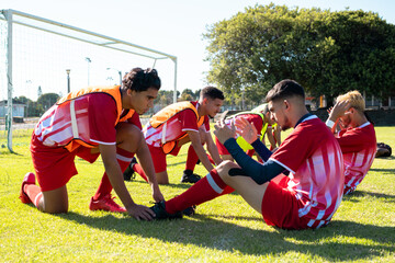 Male players holding legs of multiracial teammates practicing crunches on grassy field at playground