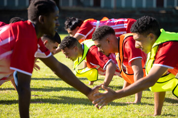 Male multiracial players in red uniforms practicing high five push-ups in a row on grassy field
