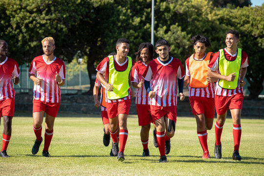 Full length of multiracial male athletes wearing red sports uniforms running in playground