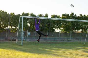 African american male goalkeeper with arms raised jumping and catching soccer ball in mid-air - Powered by Adobe